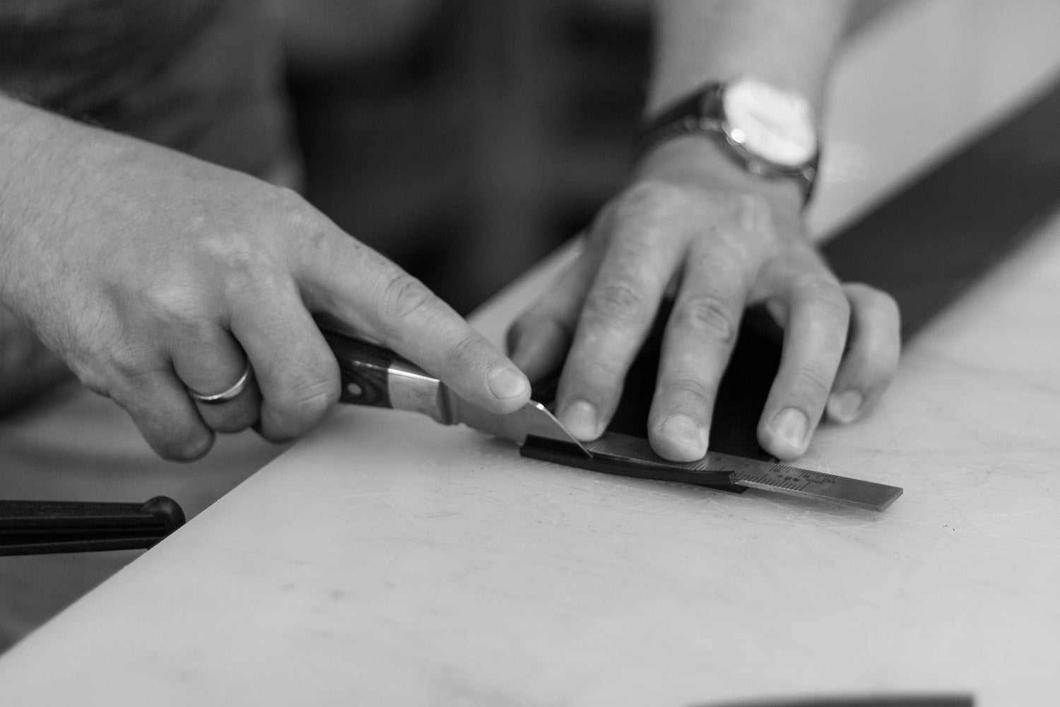 Picture of the hands of a leatherworker, using a leatherworkers knife in a leatherworkshop.